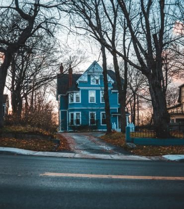 Charming blue house amid bare trees on a quiet street, evokes winter serenity.